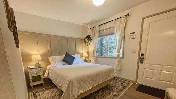 Ein Schlafzimmer mit Bett, Nachttischen, einem Fenster mit Vorhängen, einer Tür und einem Teppich.