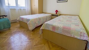 Huoneessa on kaksi erillistä sänkyä, puinen vaatekaappi, pieni yöpöytä lampun kanssa ja seinällä oleva kehystetty kuva.