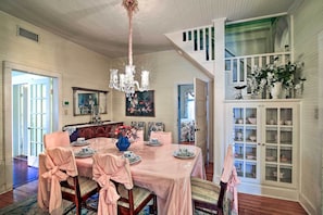 Comedor con mantel rosa, un centro de mesa floral y un mueble blanco con puertas de cristal.