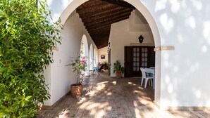 A covered outdoor corridor with arches, potted plants, and a table with chairs. - Ross Orange Apartment, Pool, Wifi (Faro)