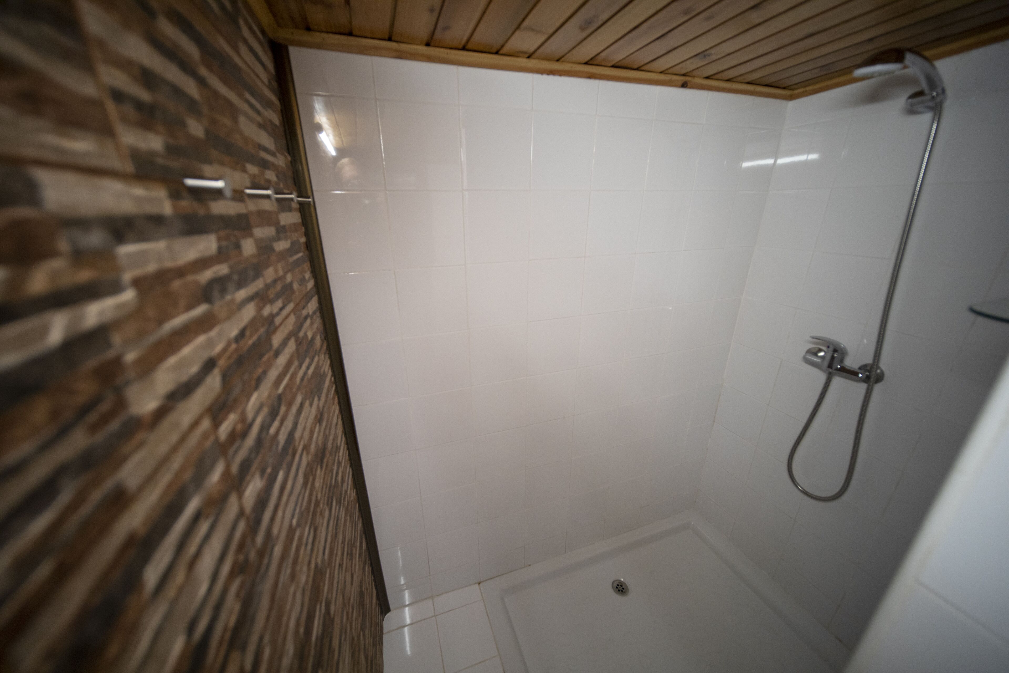 A shower with a wooden ceiling and tiled walls.