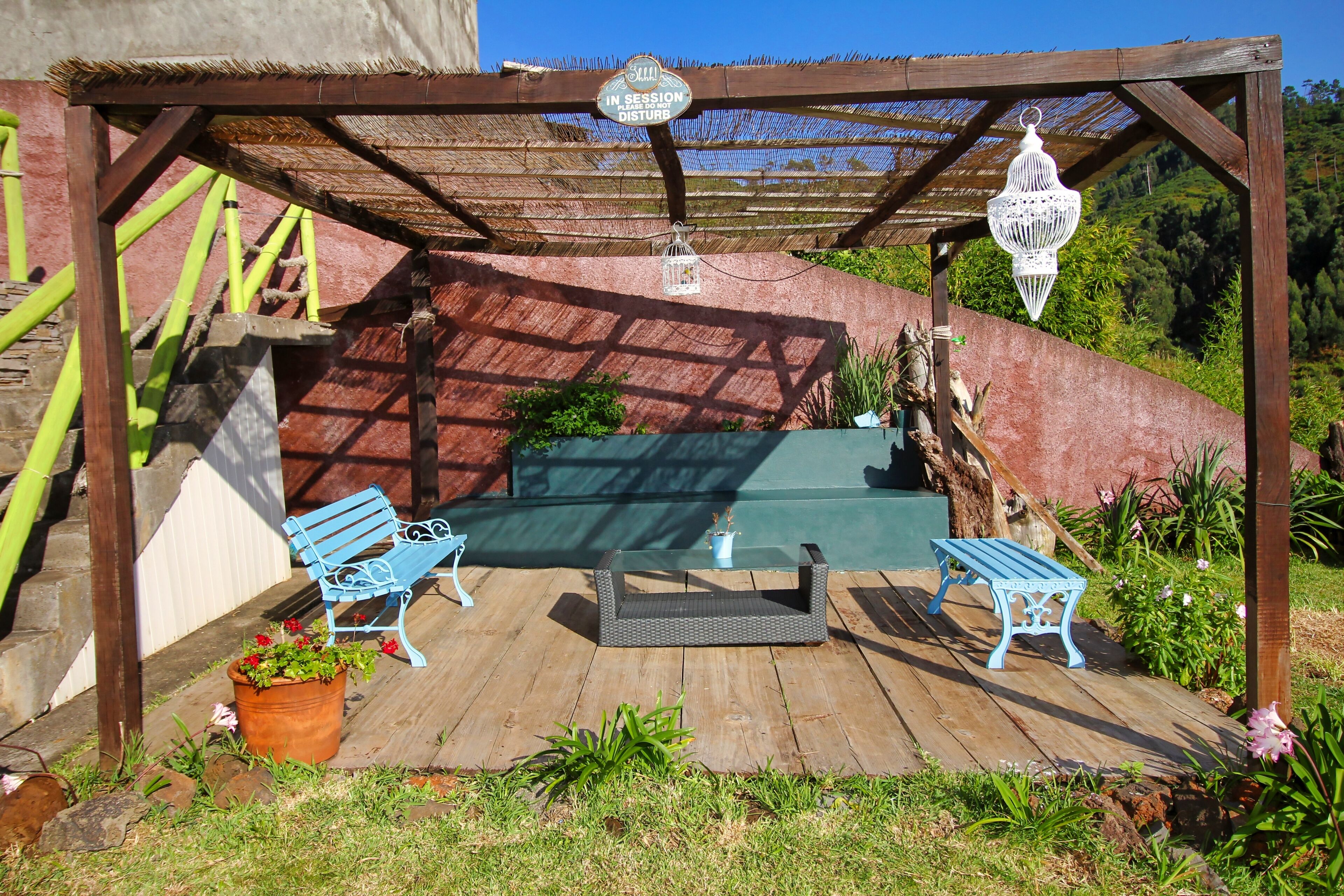 A wooden pergola with two blue benches, a small table, and a hanging birdcage.