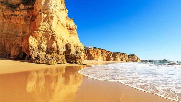 Uma praia com um penhasco imponente e um edifício no topo.