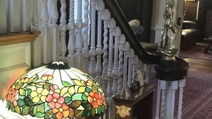 A room with a wooden table, a stained glass lamp, a magazine, and a staircase with white balusters. - Edgewood Manor (Providence)