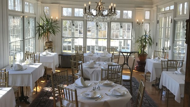 A dining area with round tables, white tablecloths, and gold chairs. - Edgewood Manor (Providence)