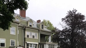 A two-story house with a green exterior and a stone wall in the foreground. - Edgewood Manor (Providence)