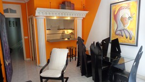 A modern living room with a dining area, featuring a white armchair, a glass coffee table, and a dining table with black chairs. - GOYA-APARTMENT-ARTS (Madrid)
