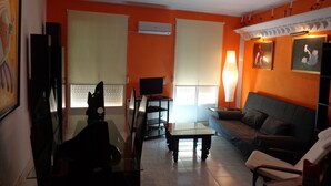 A living room with orange walls, a sofa, a coffee table, a TV, and a lamp. - GOYA-APARTMENT-ARTS (Madrid)