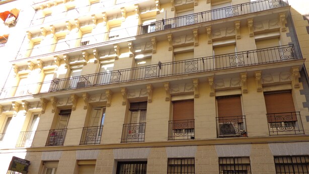 A multi-story building with balconies, large windows with metal bars, and a sign indicating a business on the ground floor. - GOYA-APARTMENT-ARTS (Madrid)