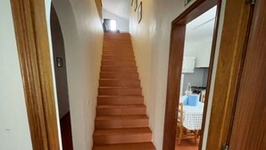 Un escalier en bois mène à une pièce où l’on aperçoit une cuisine au fond.