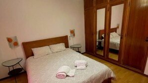 Une chambre avec un grand lit, une armoire en bois, une petite table et un luminaire suspendu.