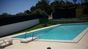 Une piscine rectangulaire avec un escalier en métal et un petit espace de terrasse agrémenté de chaises blanches.