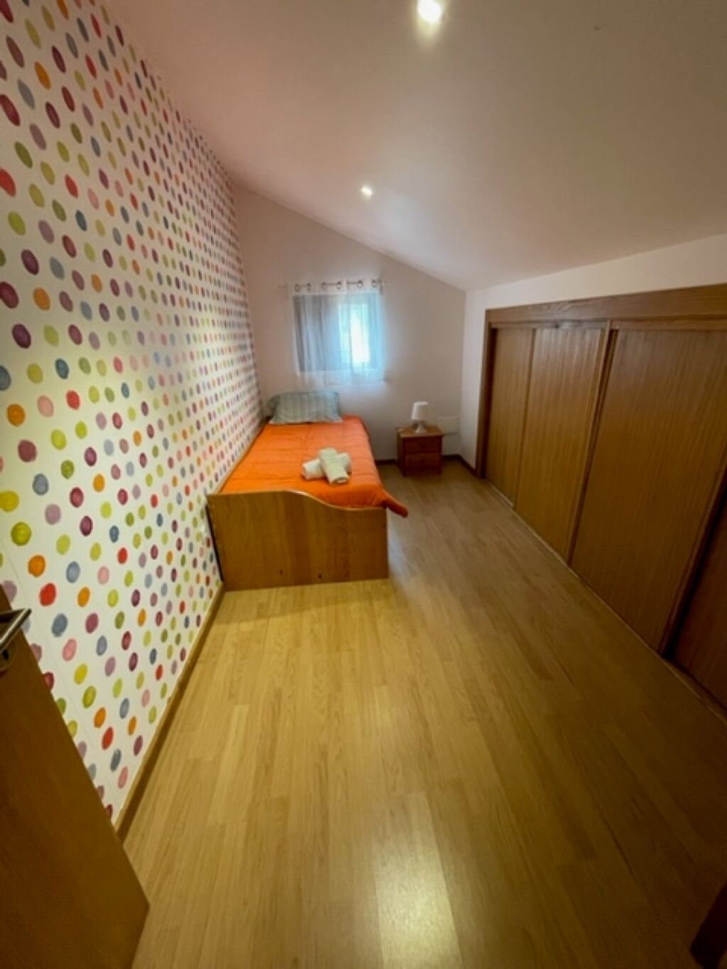 Una camera da letto con un letto, un armadio in legno e una parete a pois.