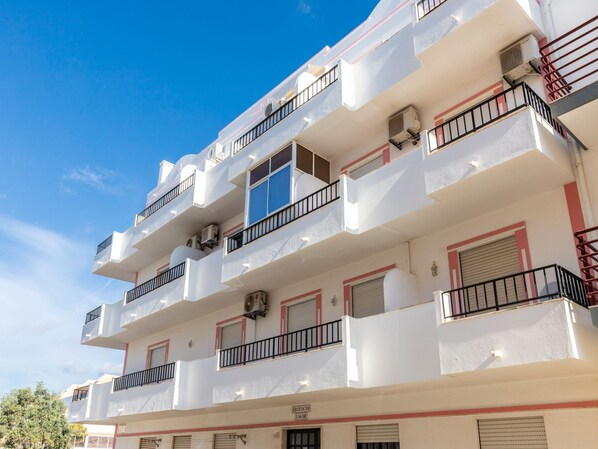 A multi-story building with balconies, air conditioning units, and a sign indicating a public space.