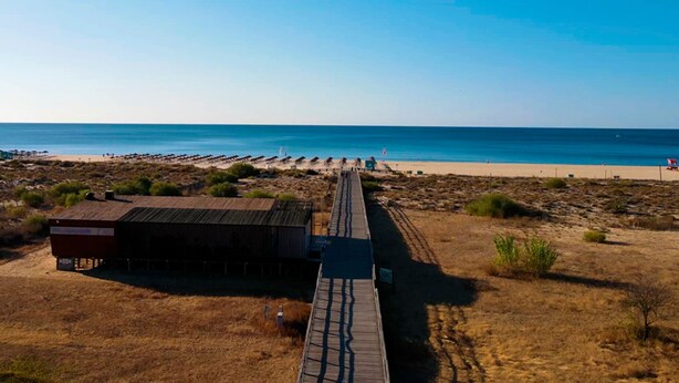 A beach with a wooden boardwalk leading to a small building.