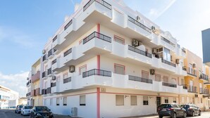 A multi-story residential building with balconies, air conditioning units, and a street view.