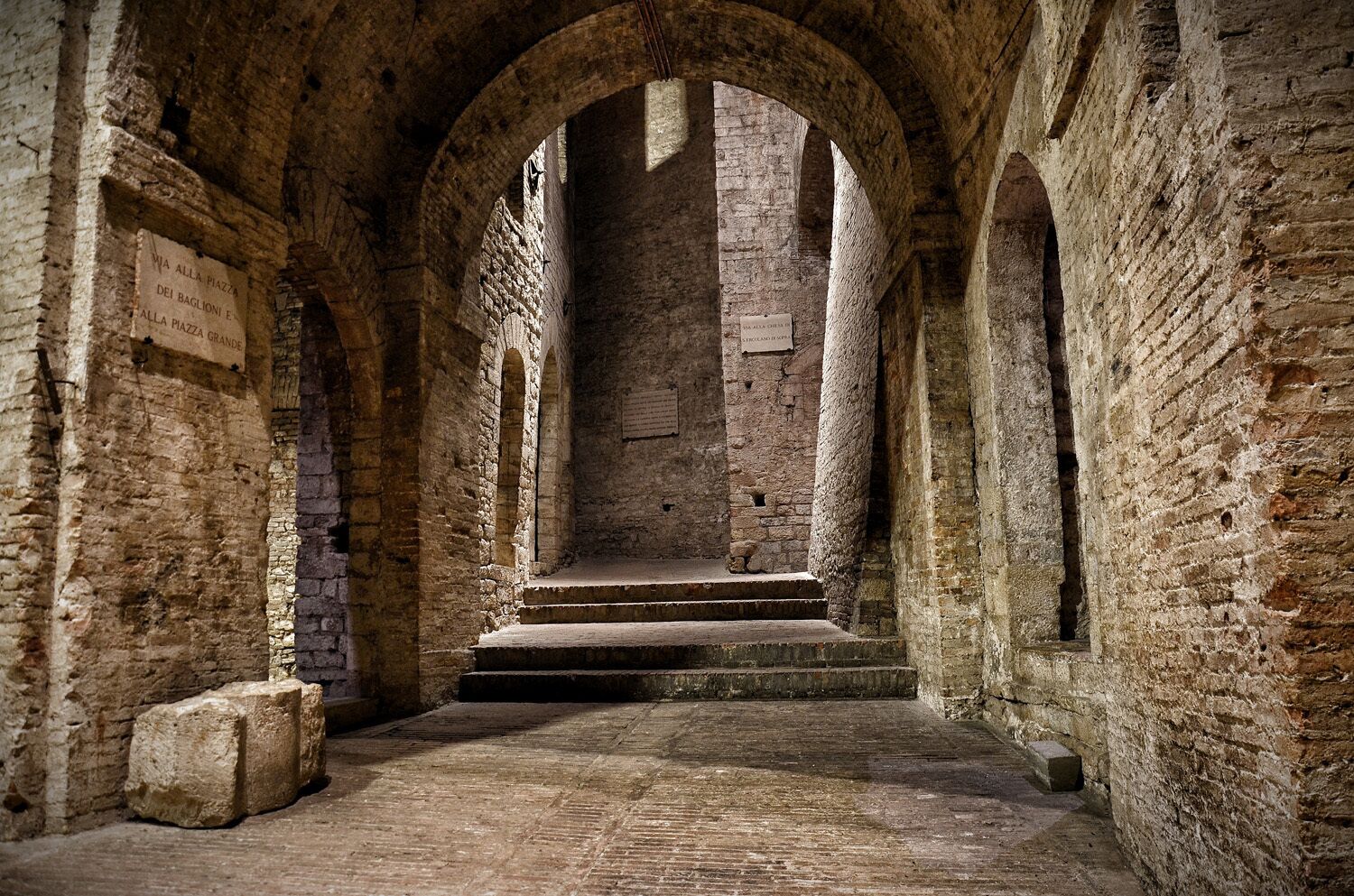 Un couloir en arc de cercle, avec des murs en pierre et des marches menant à un niveau supérieur.
