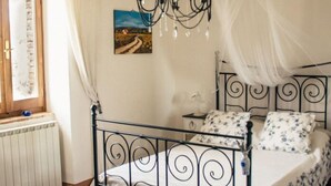 A bedroom with a metal bed frame, a canopy bed, a chandelier, a radiator, and a window with curtains.