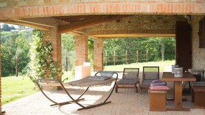An outdoor patio with a brick floor, a wooden table, a bench, and a hammock.