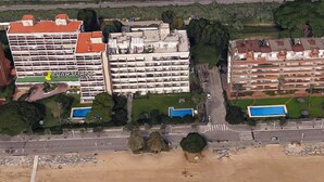 Vista aérea de una zona costera con playa, carretera y varios edificios, incluyendo un hotel de varios pisos con balcones.