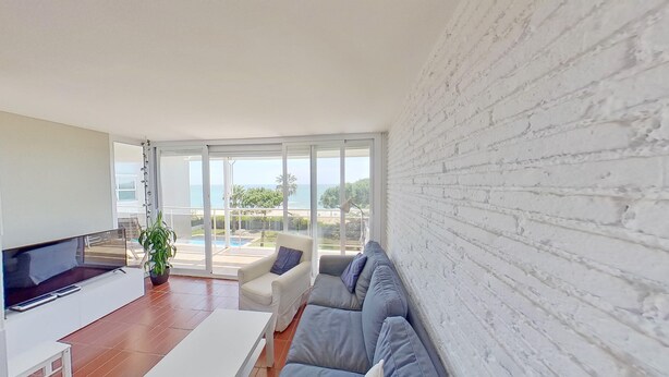 Una sala de estar moderna con una televisión de pantalla plana, un sofá y una mesa de centro. Una ventana grande ofrece vistas al mar.