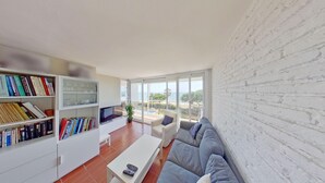 Una sala de estar moderna con una pared de ladrillo blanco, un ventanal con vistas al mar, un sofá, una mesa de centro y una estantería llena de libros.