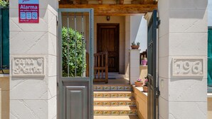 Un ingresso di un edificio con una porta in legno, un cartello che indica un sistema di allarme e il numero '196' sul muro.