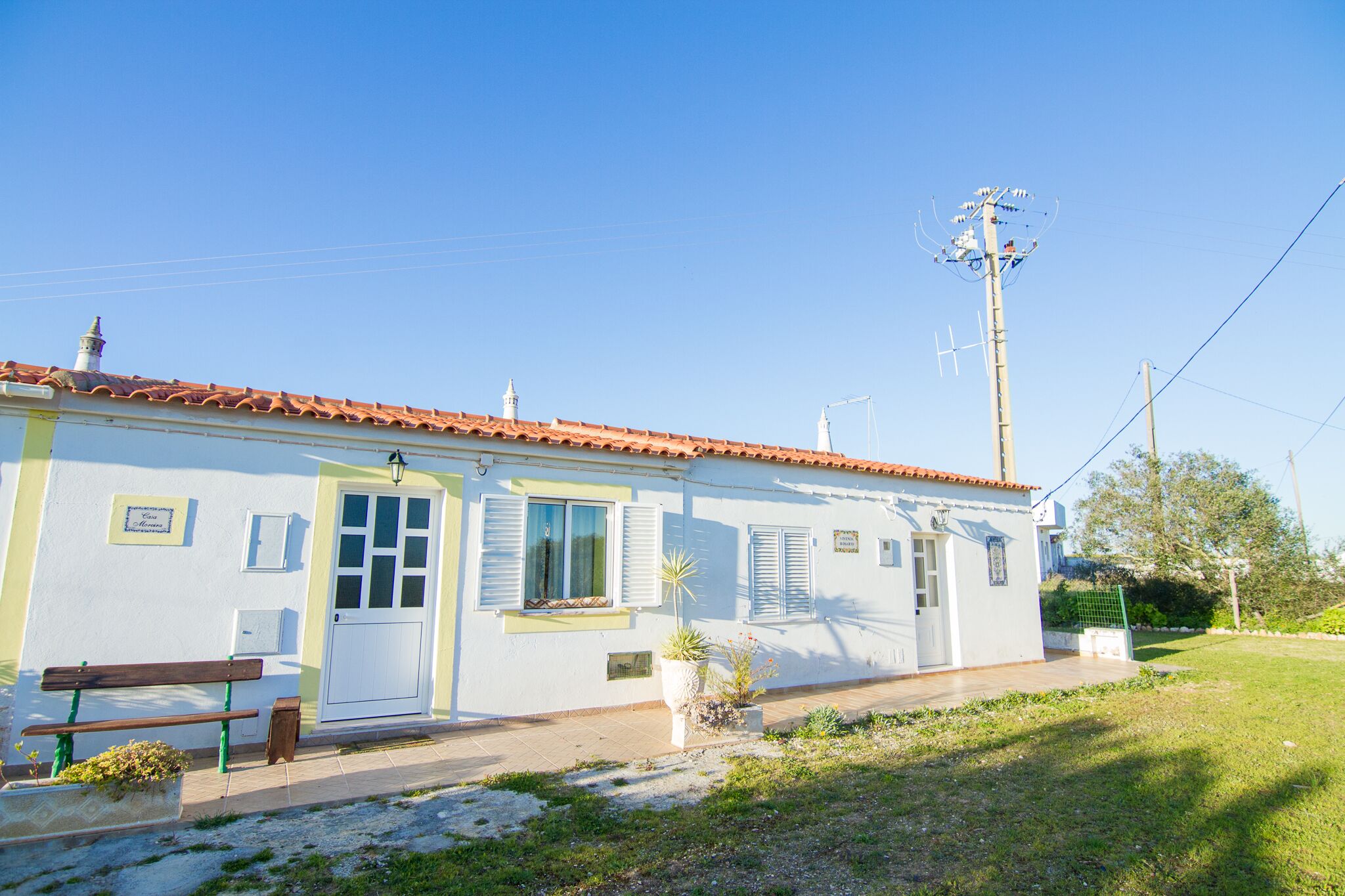A small, single-story building with a tiled roof, a bench, and potted plants.