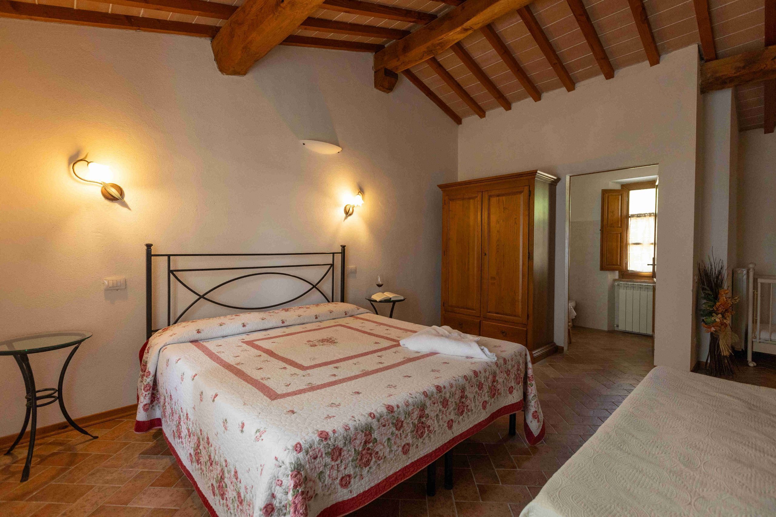 Une chambre à coucher comprenant un lit, une armoire en bois, une petite table et deux lampes fixées au mur.