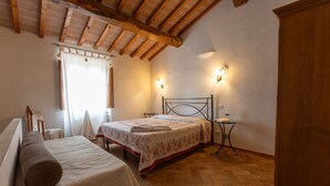 Un dormitorio con cama, mesita de noche, una pequeña mesa con lámpara y ventana con cortinas.