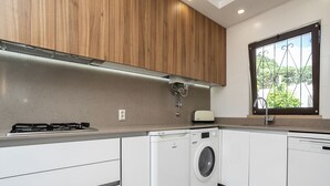 A modern kitchen with a gas stove, washing machine, and dishwasher, wooden cabinets, and a window with a view. - Feta Villa, Pool, BBQ (Olhos de Água)