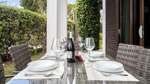 A dining table set for four with wine glasses, plates, and cutlery, surrounded by wicker furniture, under a white structure with greenery in the background. - Feta Villa, Pool, BBQ (Olhos de Água)