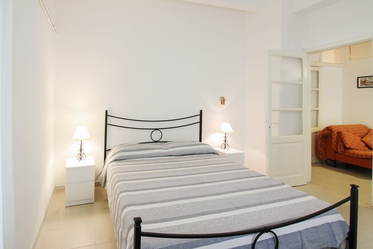 Una camera da letto con un letto, due comodini con lampade, un armadio e una porta che dà su un'altra stanza.
