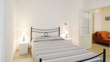 Una camera da letto con un letto, due comodini con lampade, un armadio e una porta che dà su un'altra stanza.