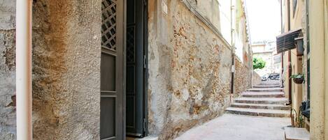 A narrow alleyway with a building entrance, a visible pipe, and a staircase leading to another level.