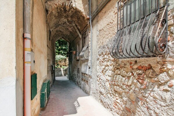 Une ruelle étroite aux murs de pierre, avec une rambarde métallique sur la droite et une porte verte sur la gauche.