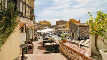 Un vicolo stretto con tavolini all'aperto, edifici in pietra e una struttura simile a un castello sullo sfondo.