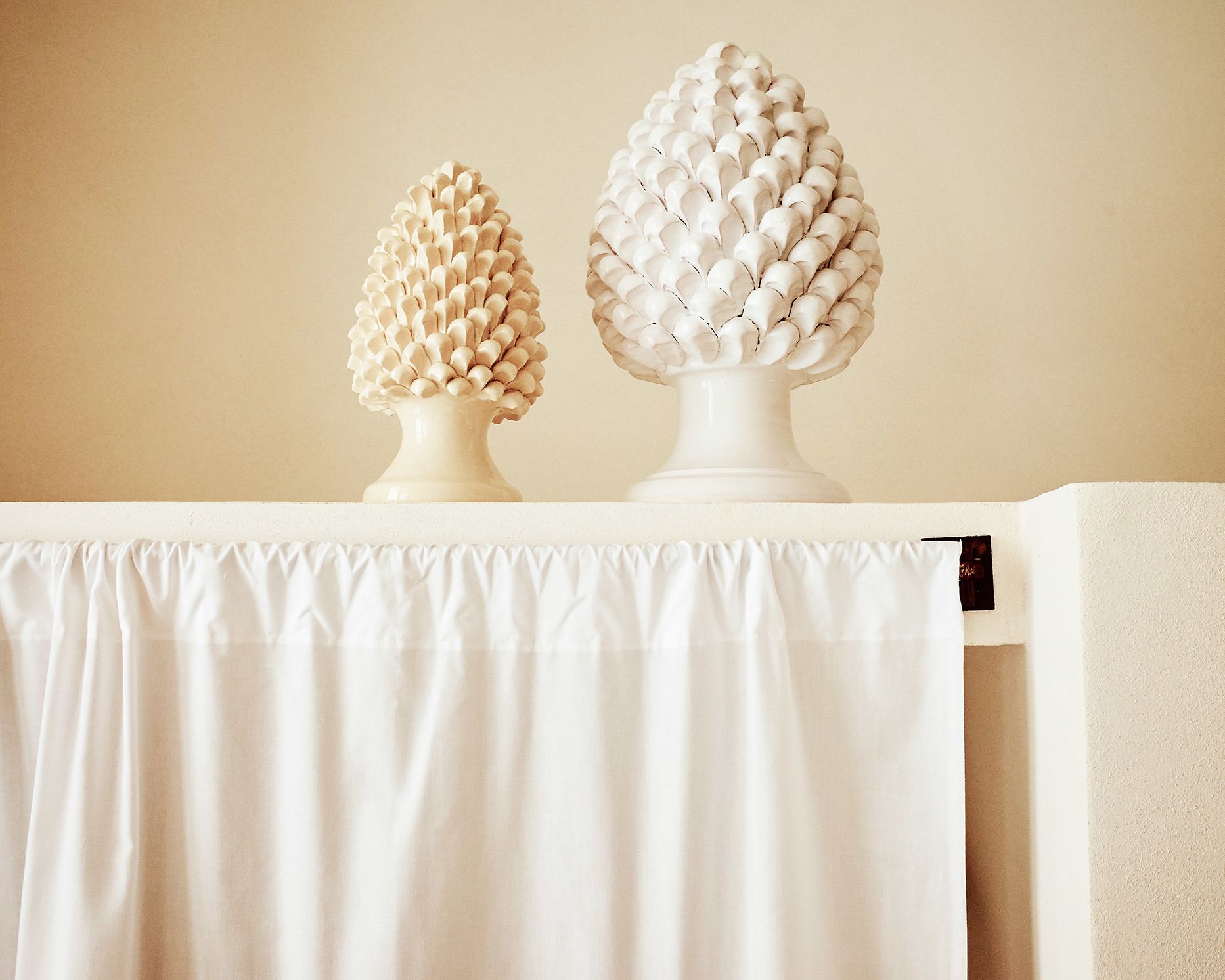 Two white decorative vases on a white table against a beige wall.