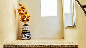 Un petit espace carrelé, agrémenté d’un vase décoratif contenant des fleurs jaunes, d’une fenêtre et d’une porte dotée d’une poignée en métal.