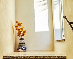 Un pequeño espacio con baldosas, un jarrón decorativo con flores amarillas, una ventana y una puerta con pomo metálico.