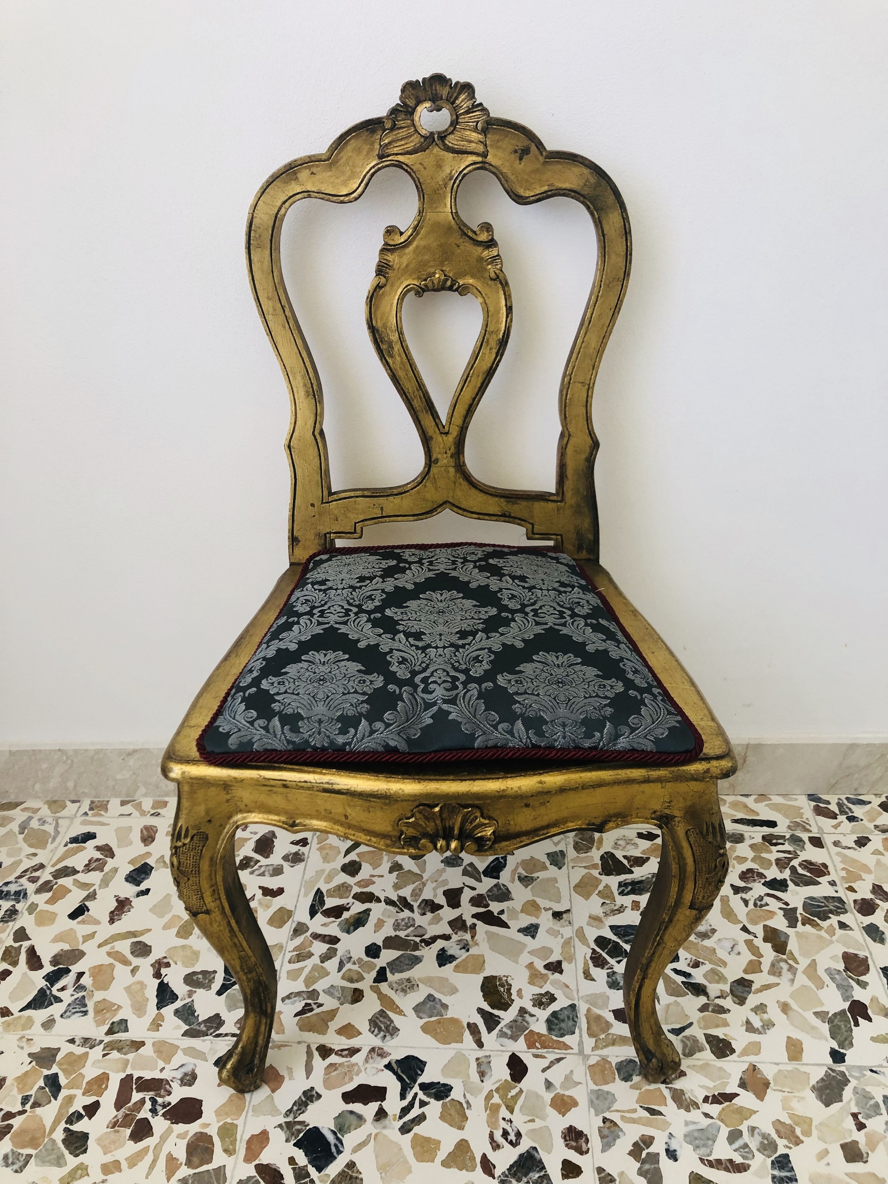 A chair with a gold frame and a patterned cushion, placed on a terrazzo floor.