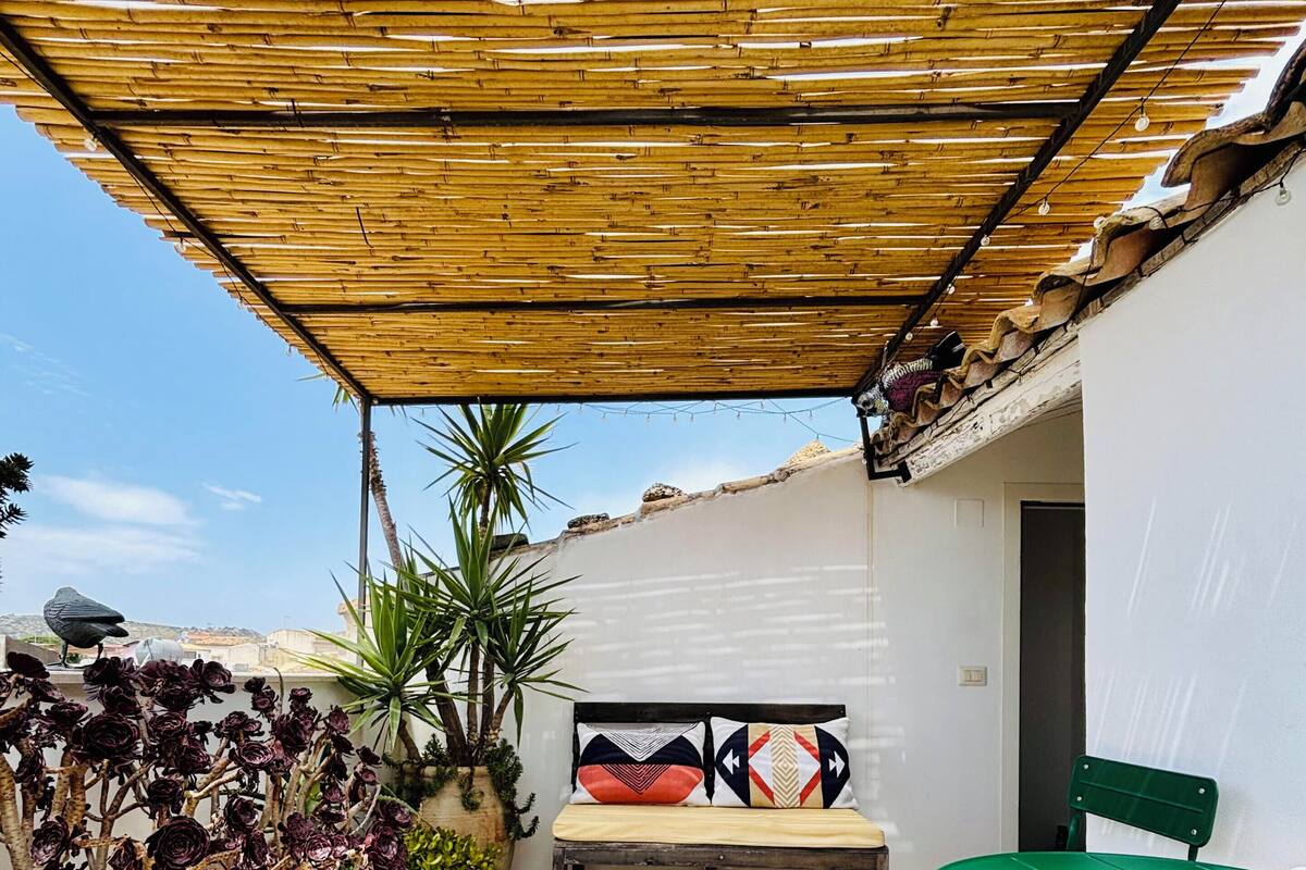 Ein überdachter Patio-Bereich mit einer Bank, einem Tisch und Blumentöpfen.