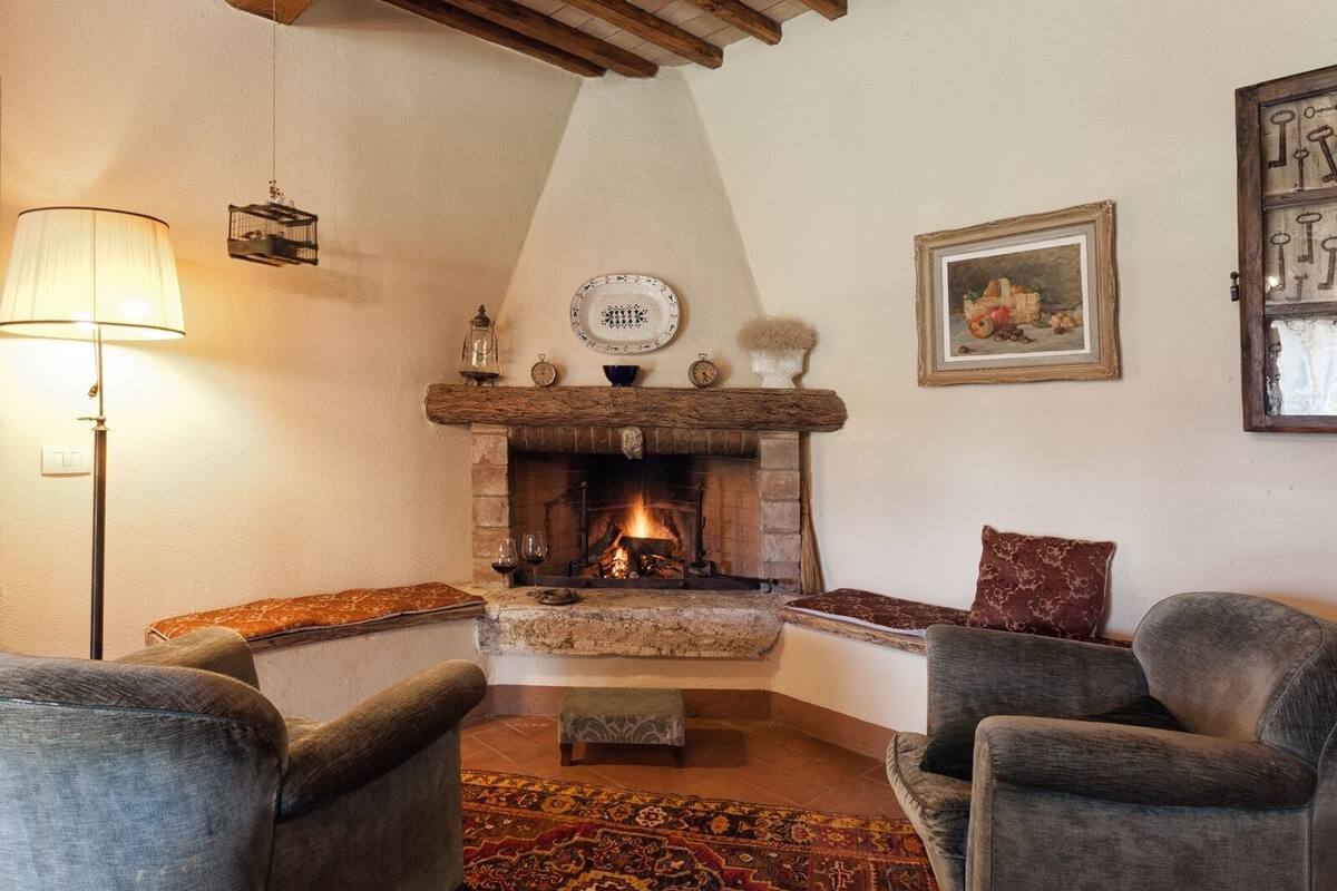 Una sala de estar acogedora con chimenea, dos sillones, un tapete estampado y una lámpara.