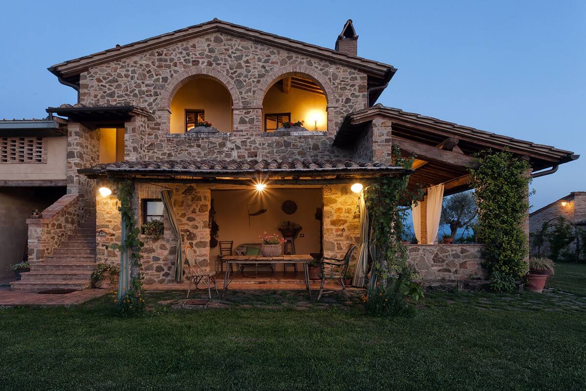 Una casa de piedra con un patio, dos arcos y una escalera que lleva al nivel superior.