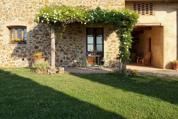 A stone building with a covered outdoor seating area, a small table, and chairs. - Agriturismo Monsole (Montalcino)