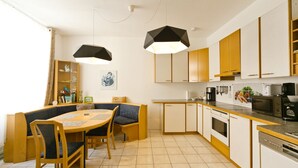 A compact kitchen with a dining area, featuring a round table, wooden chairs, and modern pendant lighting.