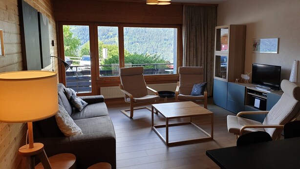 Een gezellige woonkamer met een bank, fauteuils, een salontafel, een televisie en grote ramen met uitzicht op de omgeving.