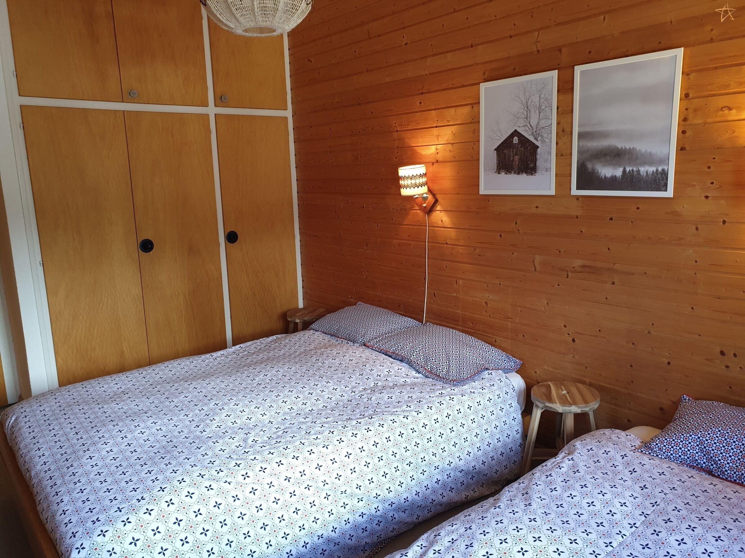 Una habitación con paneles de madera, una cama, un taburete pequeño y dos cuadros en la pared.