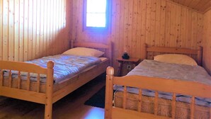 Una habitación de cabaña de madera con dos camas individuales, una mesita y una ventana.