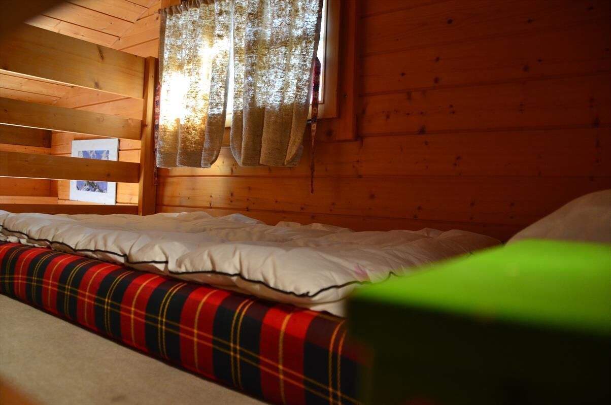 Ein Zimmer einer Holzhütte mit einem Bett, einem Fenster mit Vorhängen und Blick nach draußen.